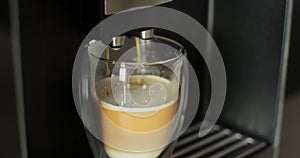 Close up coffee pouring into glass cup with milk, making cappuccino using the automatic coffee machine. Hot coffee drink