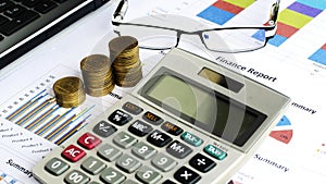 Close up of Coins stack and calculator and labtop with eyeglasses on financial chart backgrounds