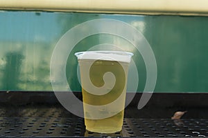 Close up of cold beer in plastic glass on green background