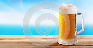 Cold mug of beer on a wooden table on background of the sea