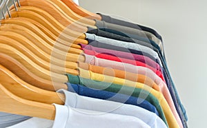 Close up collection of color t-shirts hanging on wooden clothes hanger in closet or clothing rack over white background