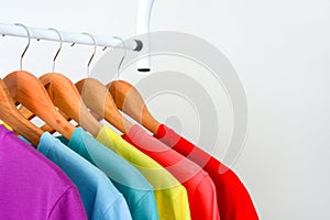 Collection of colorful rainbow t-shirts hanging on wooden clothes hanger on clothing rack over white background