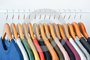 Close up collection of colorful t-shirts hanging on wooden clothes hanger in closet or clothing rack over white background