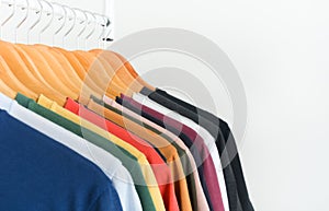 Close up collection of colorful t-shirts hanging on wooden clothes hanger in closet or clothing rack over white background, copy