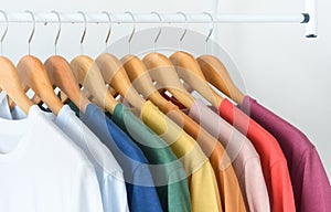 Close up collection of colorful t-shirts hanging on wooden clothes hanger in closet or clothing rack over white background, copy