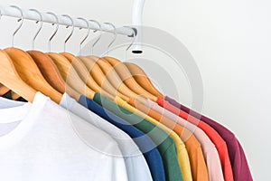 Close up collection of colorful t-shirts hanging on wooden clothes hanger in closet or clothing rack over white background, copy