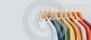 Close up collection of colorful t-shirts hanging on wooden clothes hanger in closet or clothing rack over white background, copy