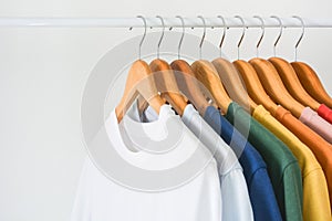Close up collection of colorful t-shirts hanging on wooden clothes hanger in closet or clothing rack over white background, copy