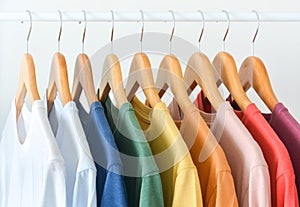 close up collection of pastel color t-shirts hanging on wooden clothes hanger in closet or clothing rack over white background