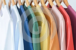 Close up collection of pastel color t-shirts hanging on wooden clothes hanger in closet or clothing rack over white background