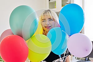 Close up of colored balloons and happy smiling face of blonde teen female