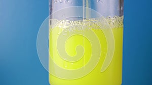 Close-up of a colored, chemical liquid pouring into a glass measuring flask on a blue background. Concept of experience