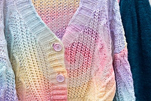 Close up of colorful knitted sweaters with buttons. Bunch of clothes of different colors for sale.