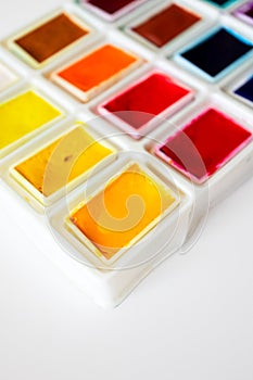 Close-up colorful watercolor palette box with selective focus on white background, top view. Concept creative