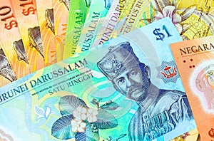 Close-up of colourful brunei dollar banknotes in various value $1, $5, $10, $100 over white. Focus on banknotes
