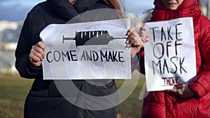 Close-up Come and make banner in hands of female activist with woman walking from background with Take off mask placard