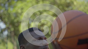 Close-up of concentrated African American sportsman throwing ball into basketball hoop. Portrait of determined young man