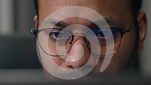 Close up concentrated focused male eyes in eyeglasses looking at laptop monitor screen light reflection in glasses man