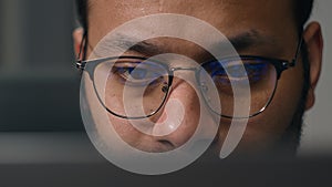 Close up concentrated focused male eyes in eyeglasses looking at laptop monitor screen light reflection in glasses man