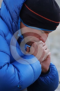 Close up of a concentrated and pensive mountain climber in thick down jacket lost in thought