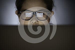 Close-up of concentrated tired Asian woman in glasses looking at computer screen while working indoor at night. Woman surfing Inte