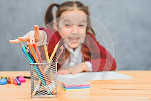 Close-up concept of multicolored pencils on the table on the mistress background of the girl. A schoolgirl stretching