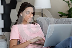 Close up confident Arabian woman using laptop, relaxing on couch