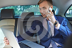 Confident businessman talking on mobile phone sitting in the back seat of a car