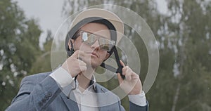 Close-up of confident handsome man in sunglasses putting on biking helmet under rain. Portrait of Caucasian biker