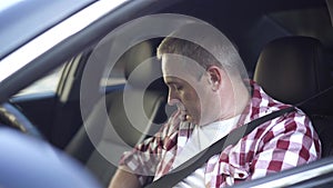 Close-up of confident middle aged Caucasian man fastening seat belt sitting on driver's seat and turning on engine