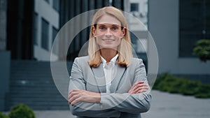 Close-up confident successful young businesswoman in formal suit posing with crossed arms outdoors smiling ambitious