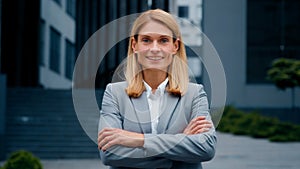 Close-up confident successful young businesswoman in formal suit posing with crossed arms outdoors smiling ambitious