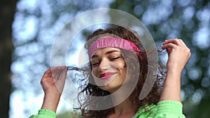 Close-up confident young woman in hair band looking away smiling standing outdoors in summer park. Portrait of beautiful