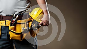Close up of construction worker holding tool belt and helmet on brown background