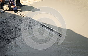 Close up of construction worker`s gloved hands using trowel to scrape excess mix level with wood forms freshly poured concrete pa