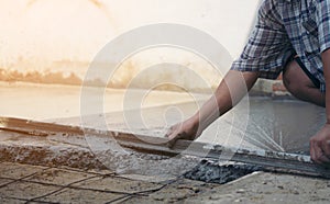 Close up of construction worker`s gloved hands using trowel to scrape excess mix level with wood forms freshly poured concrete pa