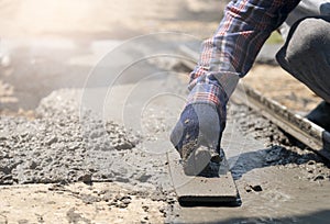 Close up of construction worker`s gloved hands using trowel to scrape excess mix level with wood forms freshly poured concrete pa