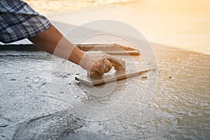 Close up of construction worker`s gloved hands using trowel to scrape excess mix level with wood forms freshly poured concrete pa