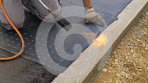 CLOSE UP: Contractor uses a blowtorch to burn a bitumen sheet to the ground.