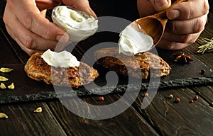 Close-up of a cook hands with a spoon for adding sour cream to meat cutlets before breakfast