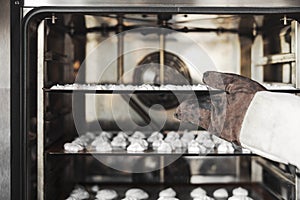 Close up of cook putting meringue cookies in the oven.