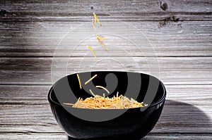 Close-up of cooked polyphosphate noodles falling into a black bowl