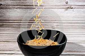 Close-up of cooked polyphosphate noodles falling into a black bowl
