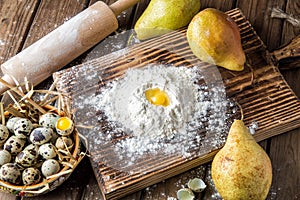 Close up. Cooking Easter cake. Yellow Egg Yolk in a hill of white flour, surrounded by ripe large pears and a bowl of pearl eggs.