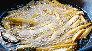 Close-up of cooking French fries in a frying pan on hot fire from gas in kitchen.