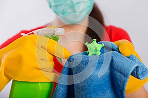 Close-up of a coronavirus model in the hands of a cleaning lady. A housewife in a mask and gloves holds a atomizer and rag.