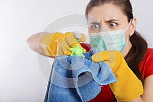Close-up of a coronavirus model in the hands of a cleaning lady. A housewife in a mask and gloves holds a atomizer and rag.