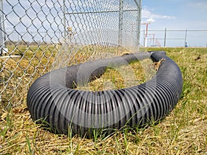 Close up of corrugated black plastic pipe on the grass. Fence and airfield landing lights.