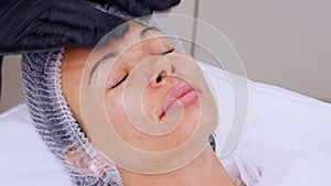 Close-up, cosmetician in black medical gloves applies cosmetic cream to female face with massage movements. skincare