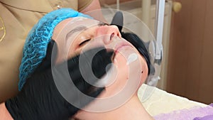 close-up, cosmetician in medical gloves applies evenly cosmetic cream or sunscreen to female face after peeling